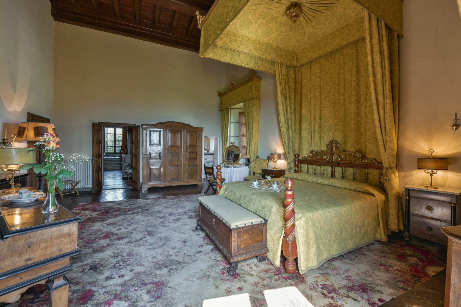 Luxurious bedroom featuring a four-poster bed with golden drapes, antique wooden furniture, and elegant decor. The room has a warm ambiance, highlighted by soft lighting and rich textures, creating a cozy and inviting atmosphere. | Only on SopranoVillas