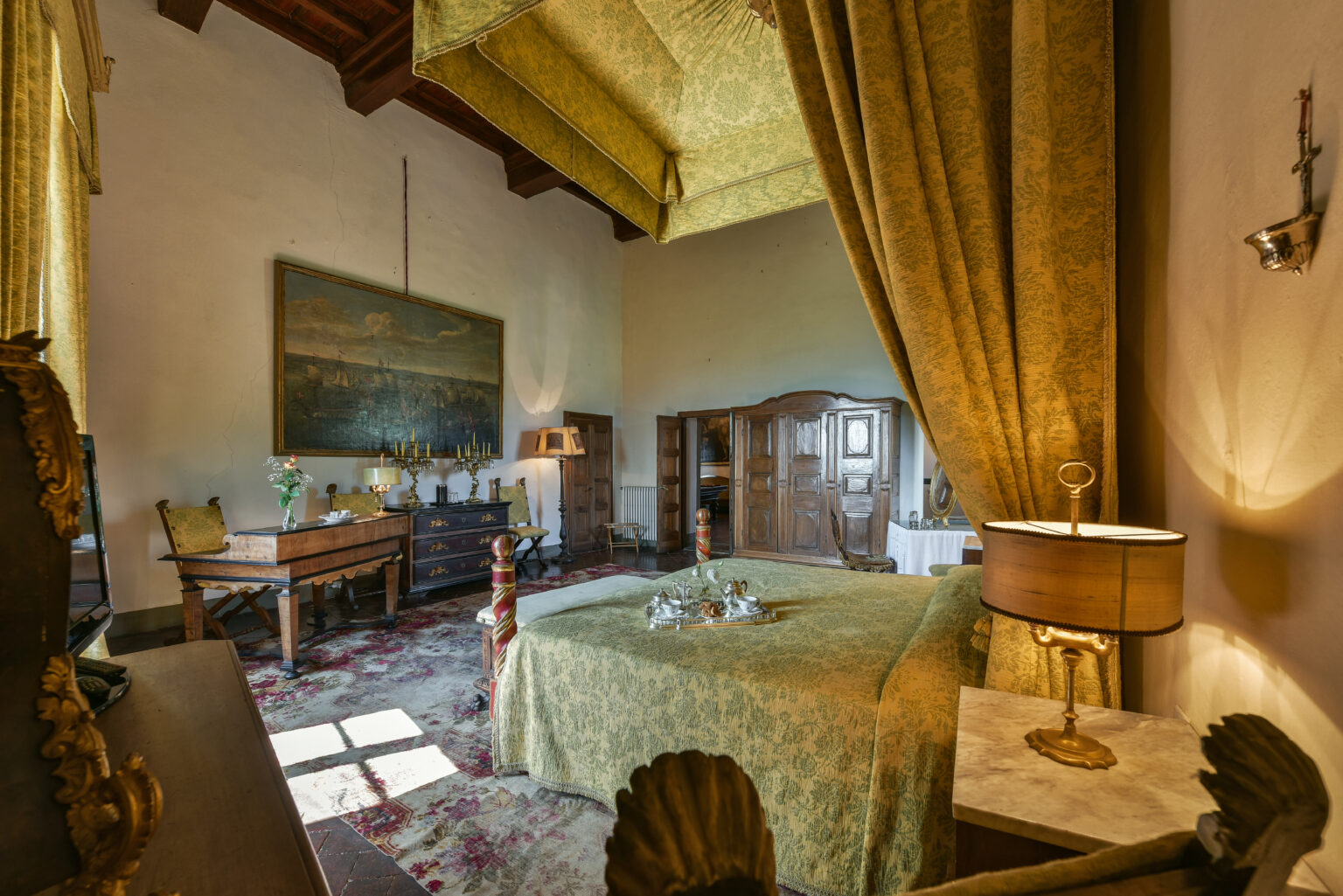 Luxurious bedroom interior featuring a canopied bed, elegant golden drapes, antique furniture, and a large painting on the wall, creating a warm and inviting atmosphere. | Only on SopranoVillas