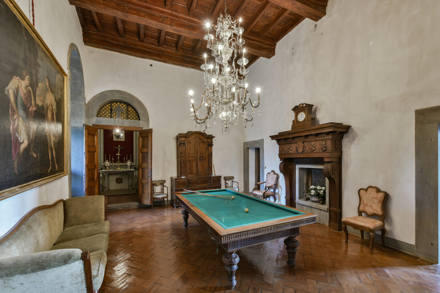 Elegant interior of a room featuring a billiard table, vintage furniture, and a grand chandelier, with wood-beamed ceilings and classic artwork on the walls. | Only on SopranoVillas