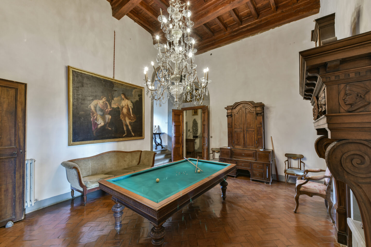 Elegant interior of a game room featuring a vintage billiard table, ornate chandelier, and classic wooden furniture, with a large painting on the wall and warm, inviting decor. | Only on SopranoVillas