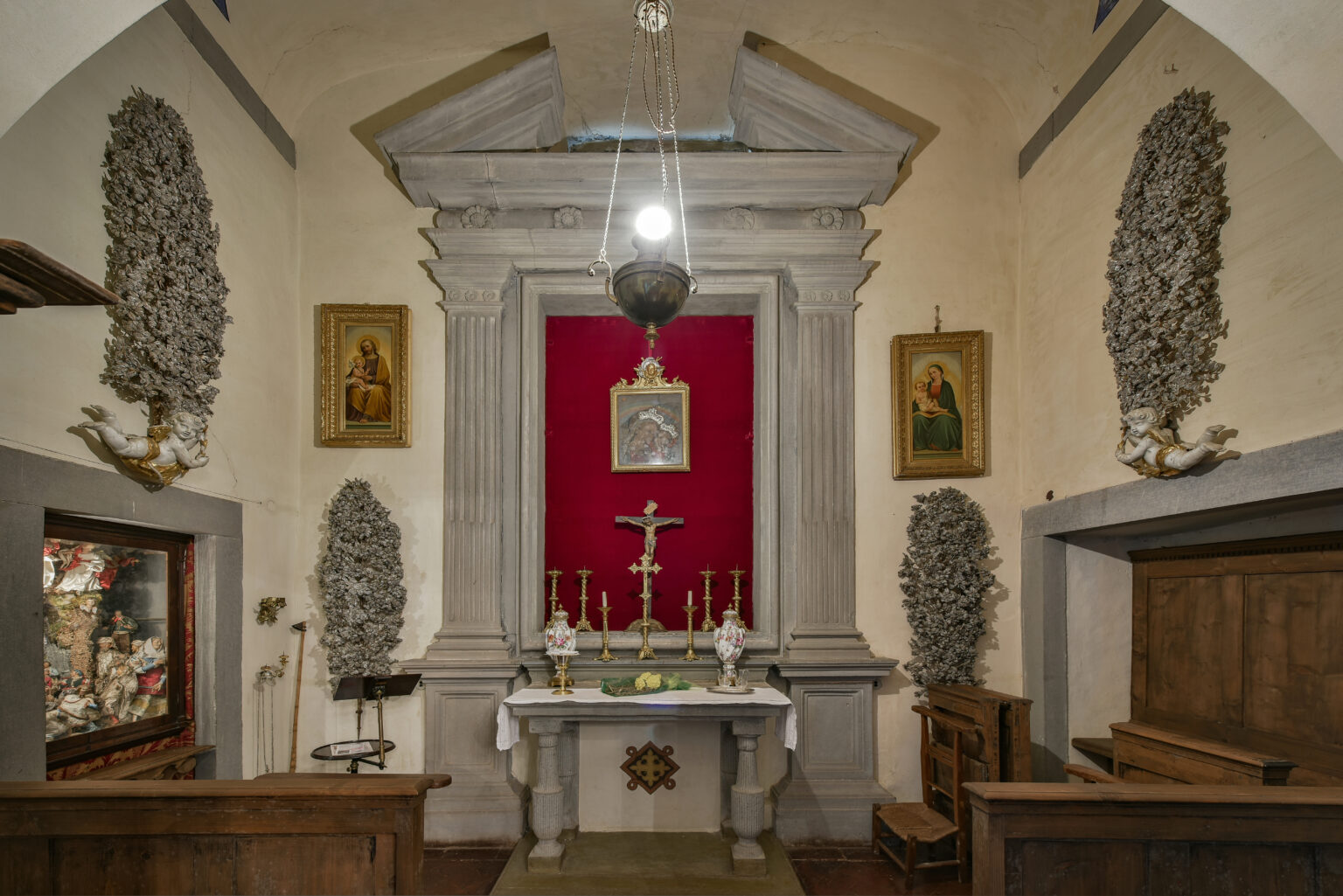 Interior view of a small chapel featuring a stone altar, red backdrop, religious artwork, and decorative wall elements, showcasing a serene and sacred atmosphere. | Only on SopranoVillas