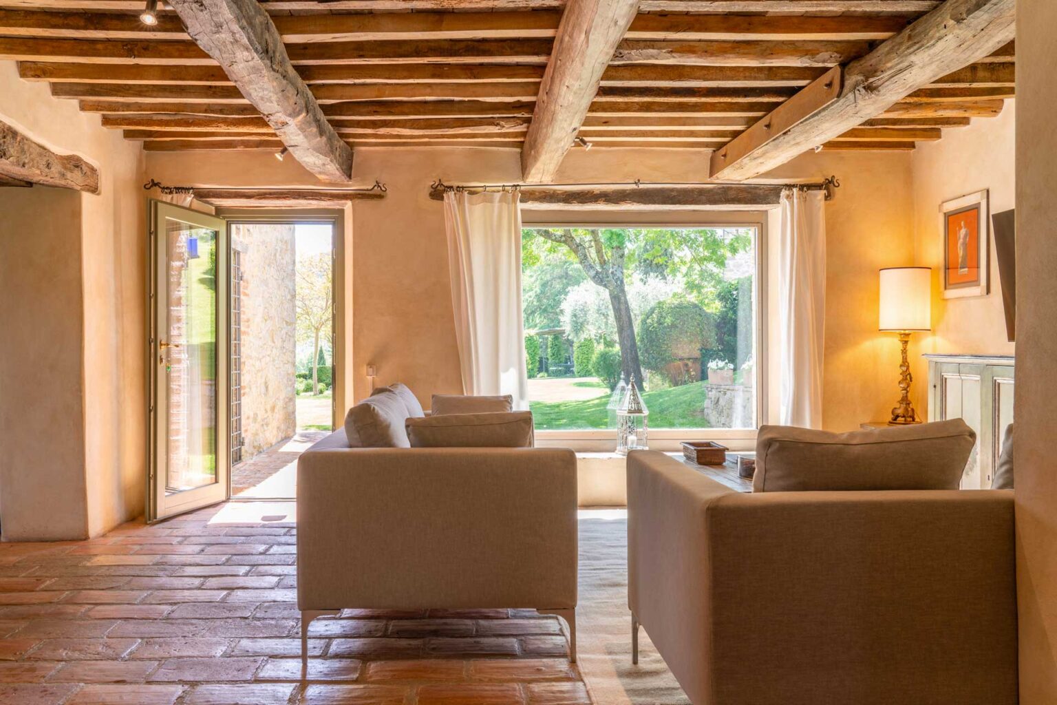 Cozy living room with wooden beams, two modern sofas, and large windows overlooking a lush garden, creating a bright and inviting atmosphere. | Only on SopranoVillas