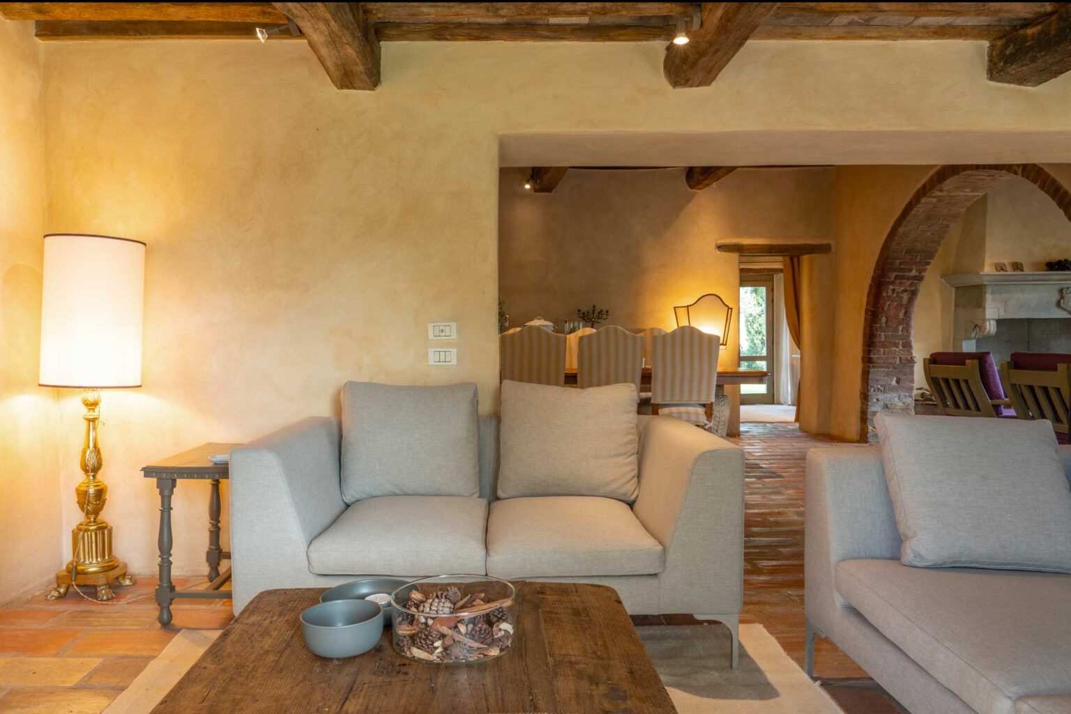 Cozy living room interior featuring a light-colored sofa, wooden coffee table, and a stylish lamp, with an arched doorway leading to a dining area in the background. Warm, inviting atmosphere with natural light. | Only on SopranoVillas