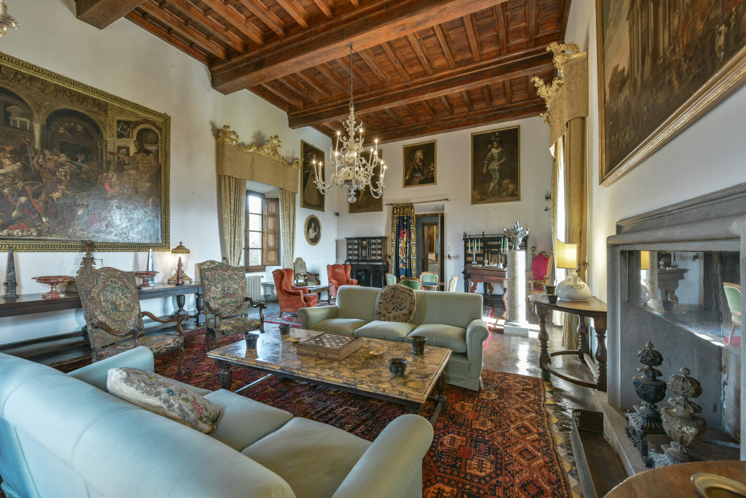 Elegant living room featuring vintage decor, ornate chandeliers, and classic artwork on the walls. The space includes comfortable seating, a decorative coffee table, and rich wooden beams on the ceiling, creating a warm and inviting atmosphere. | Only on SopranoVillas