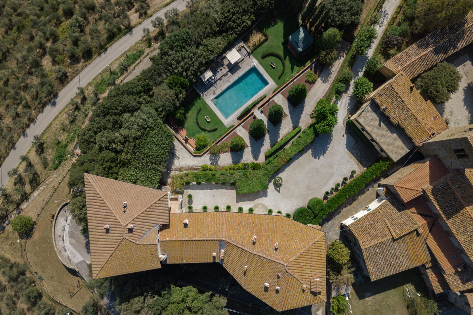 Aerial view of a luxury villa featuring a swimming pool, landscaped gardens, and surrounding olive groves. The property showcases a modern design with a spacious driveway and outdoor seating areas. | Only on SopranoVillas