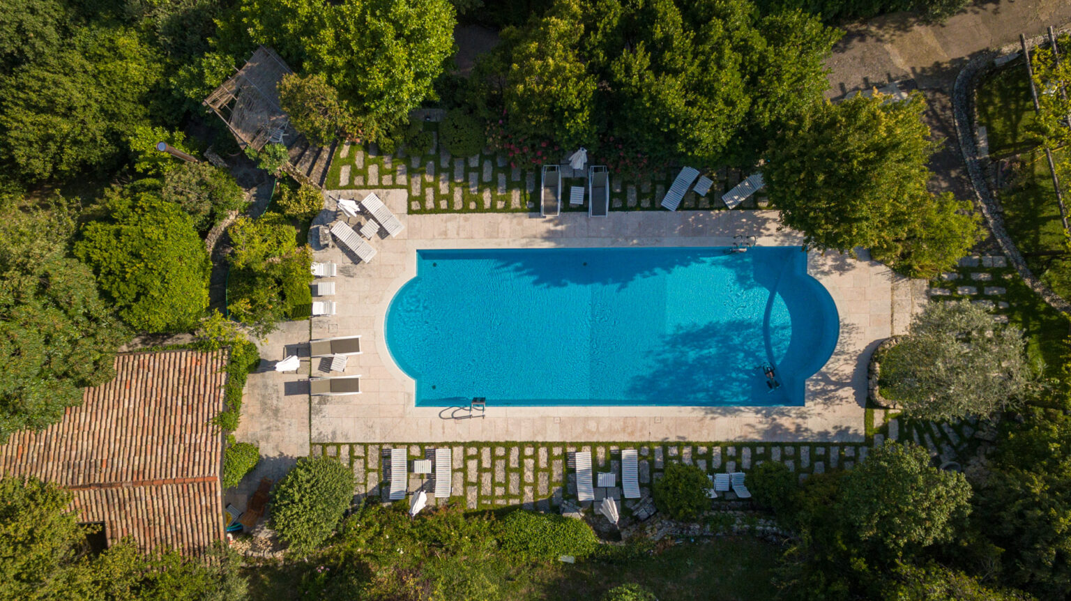 Aerial view of a serene outdoor swimming pool surrounded by lush greenery, stone pathways, and comfortable lounge chairs, ideal for relaxation and leisure in a tranquil garden setting. | Only on SopranoVillas