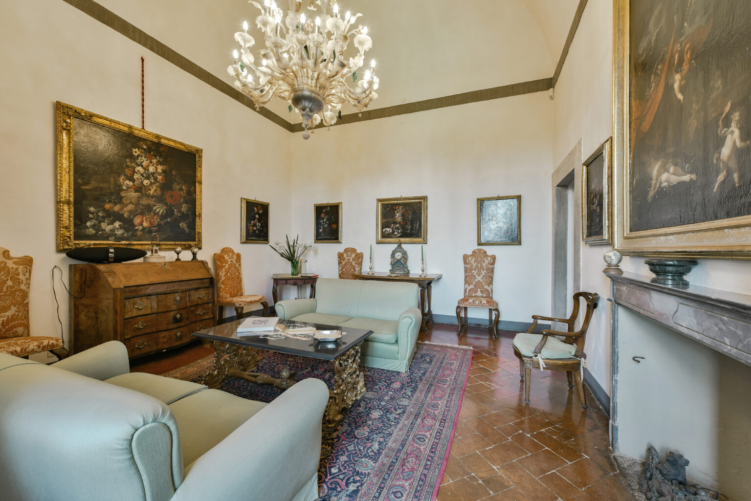 Elegant interior of a classic living room featuring a chandelier, vintage furniture, and ornate paintings on the walls, showcasing a blend of historical charm and modern comfort. | Only on SopranoVillas