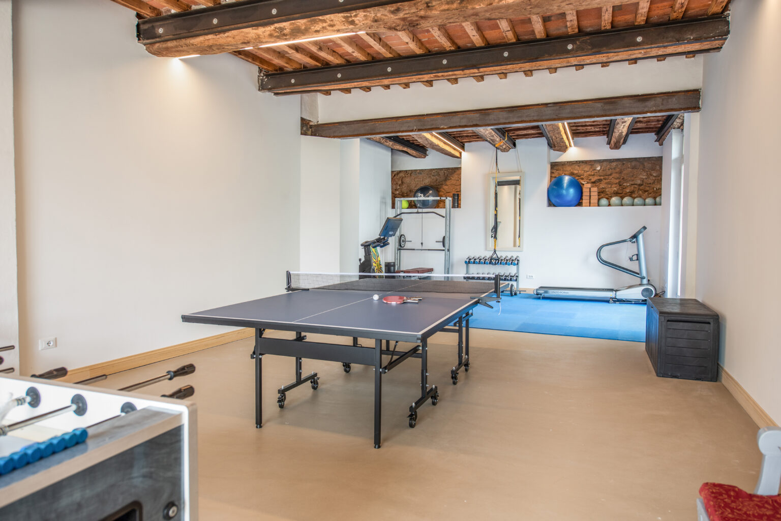 Modern home gym featuring a ping pong table, exercise equipment, and a spacious layout with wooden beams. Ideal for fitness enthusiasts and recreational activities. | Only on SopranoVillas