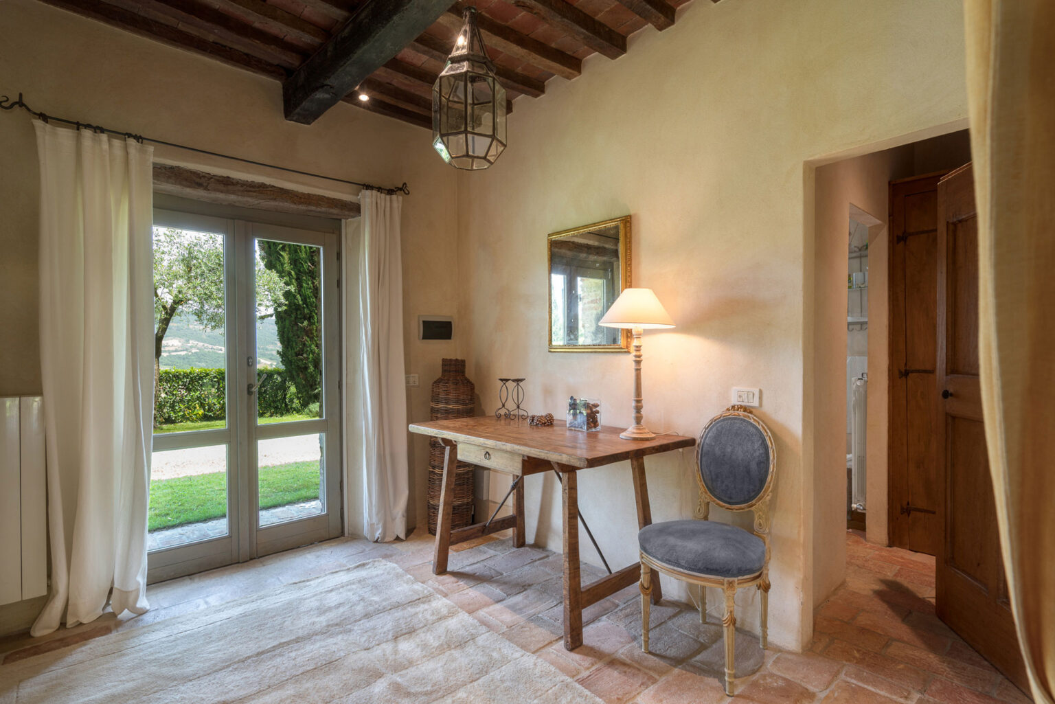 Cozy home office with a wooden desk and a blue chair, featuring natural light from large windows, rustic decor, and a warm ambiance. | Only on SopranoVillas