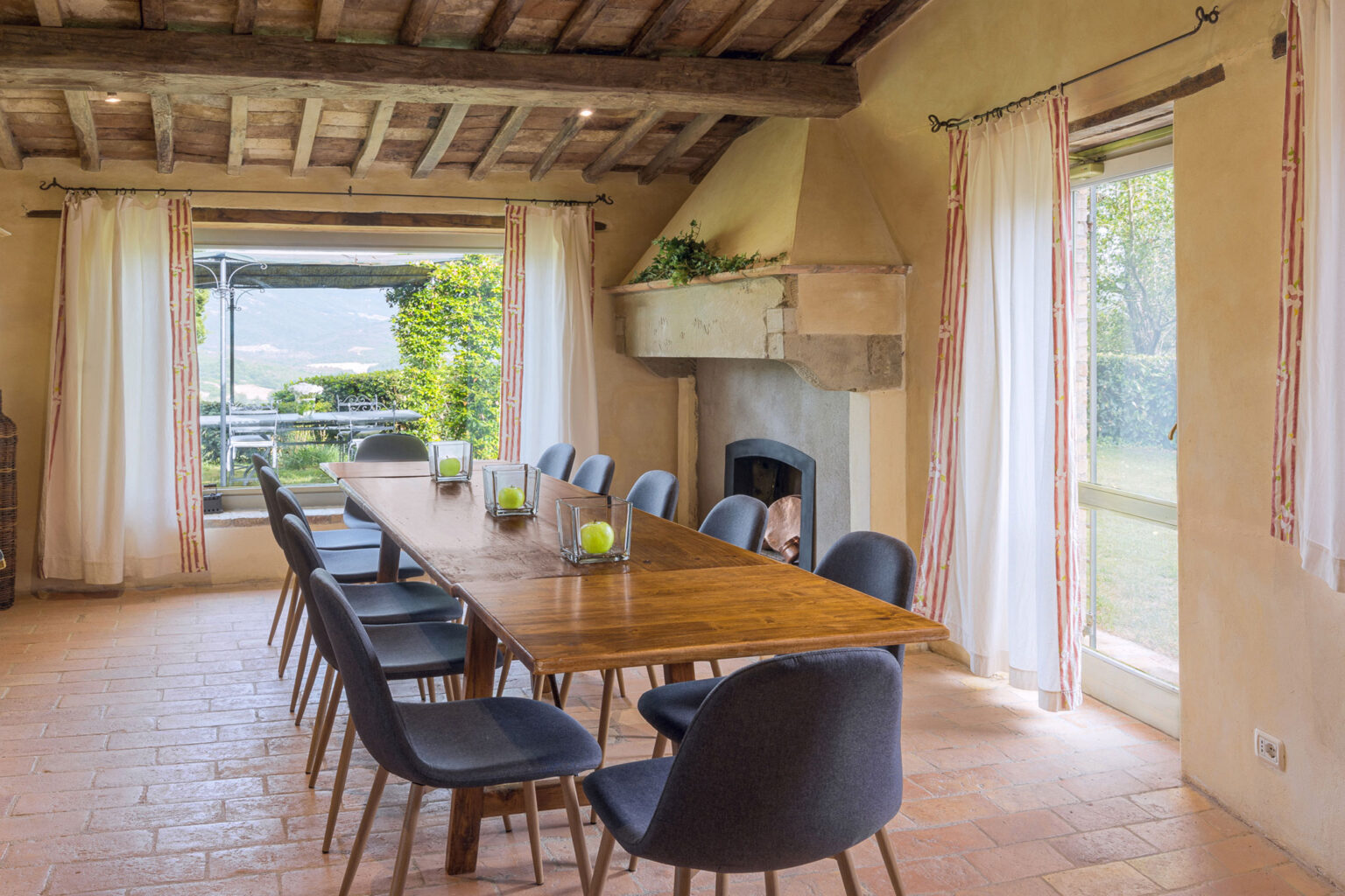 Spacious dining room with a large wooden table surrounded by modern chairs, featuring rustic decor, large windows, and a view of the garden. Ideal for gatherings and family meals. | Only on SopranoVillas