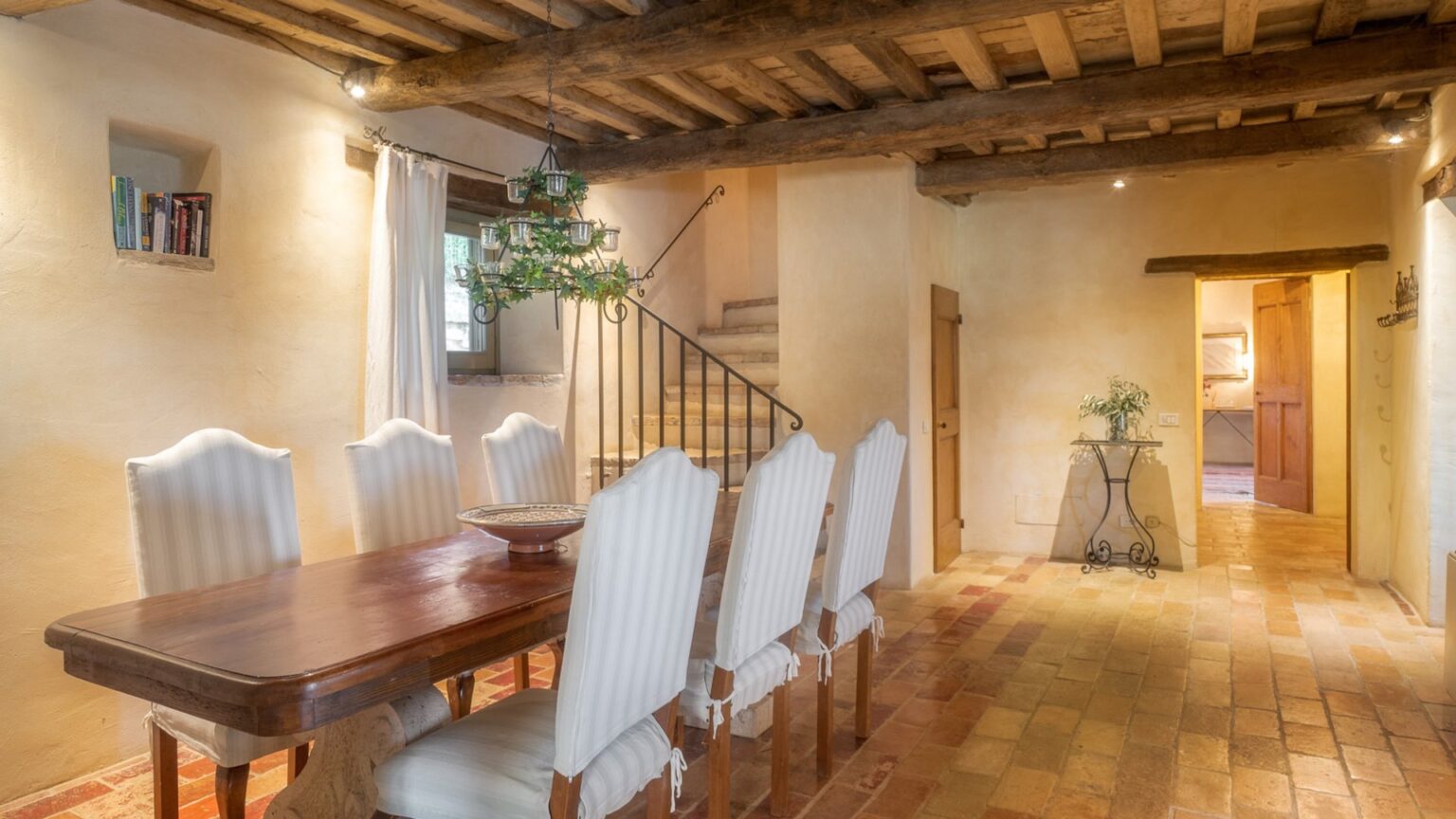 Spacious dining area featuring a wooden table and elegant white chairs, with rustic wooden beams and warm tiled flooring, creating a cozy and inviting atmosphere. | Only on SopranoVillas