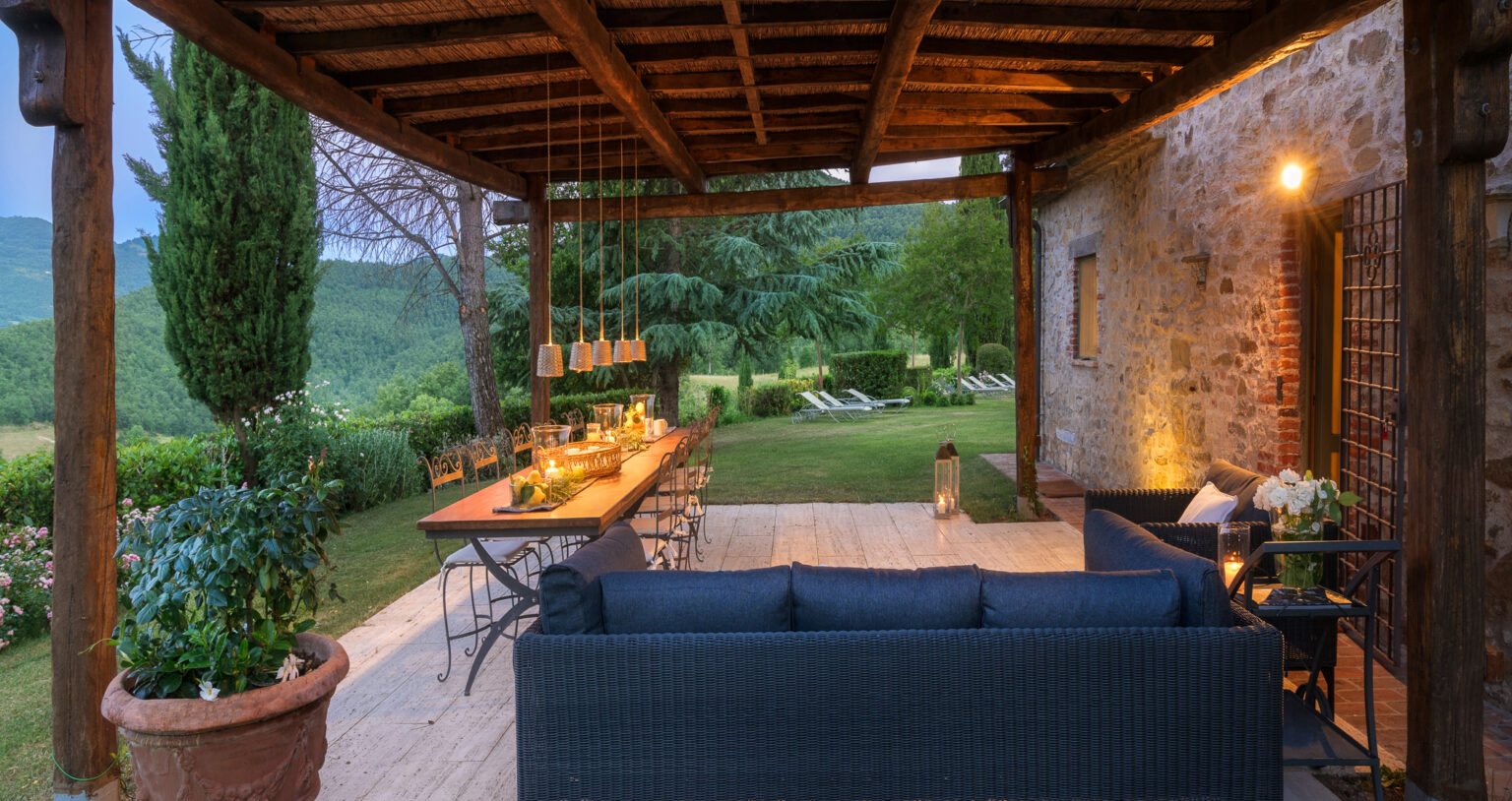 Cozy outdoor patio with a wooden pergola, featuring a long dining table, comfortable seating, and lush green views, ideal for entertaining and relaxation. | Only on SopranoVillas