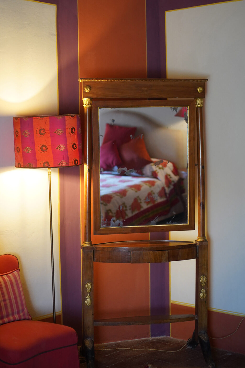 Wooden dresser with a large mirror reflecting a cozy bedroom, featuring a colorful lamp and a floral bedspread with decorative pillows. | Only on SopranoVillas