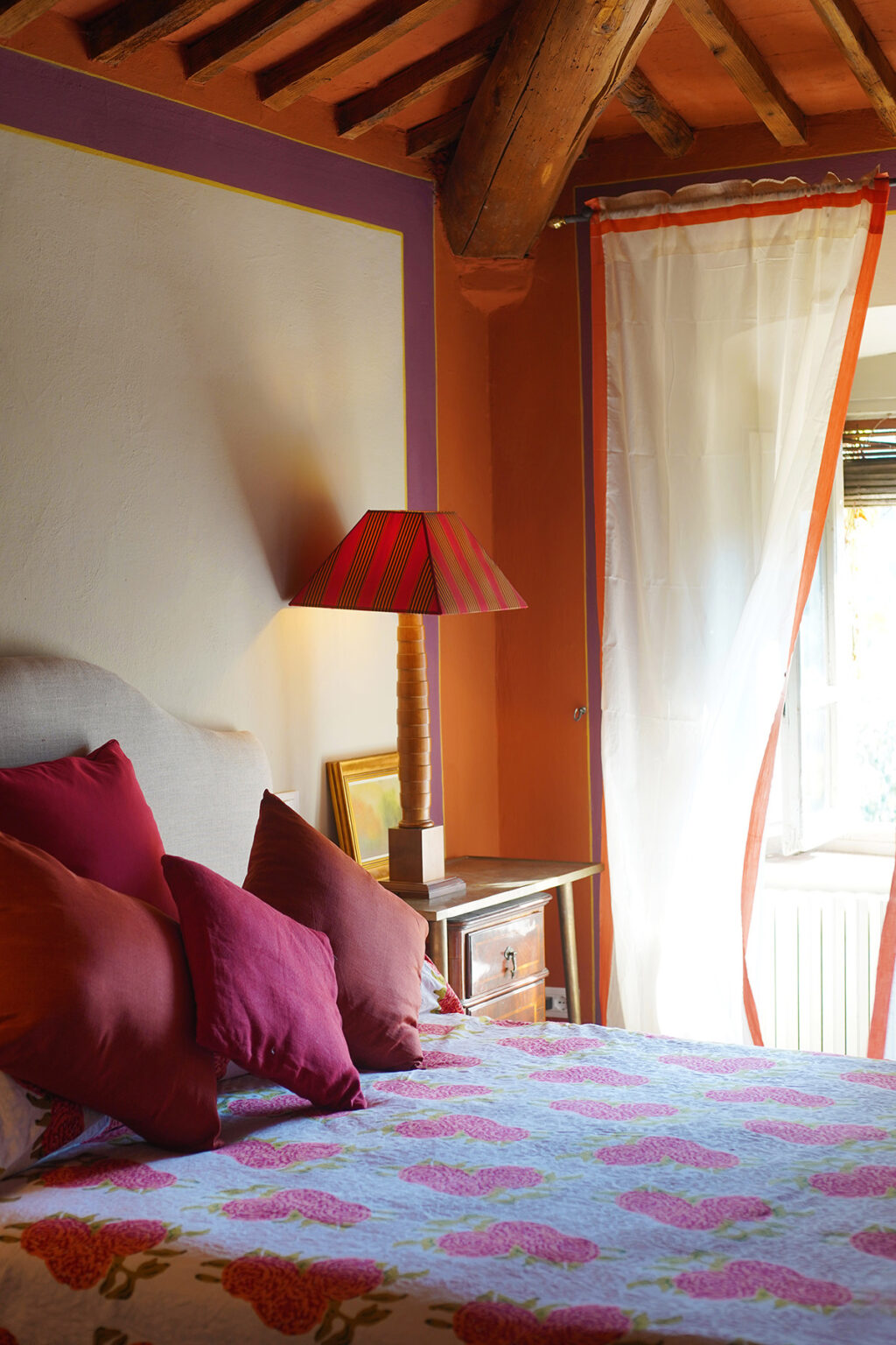 Cozy bedroom featuring a stylish lamp with a red striped shade, colorful walls in orange and purple, and decorative pillows on the bed, creating a warm and inviting atmosphere. | Only on SopranoVillas