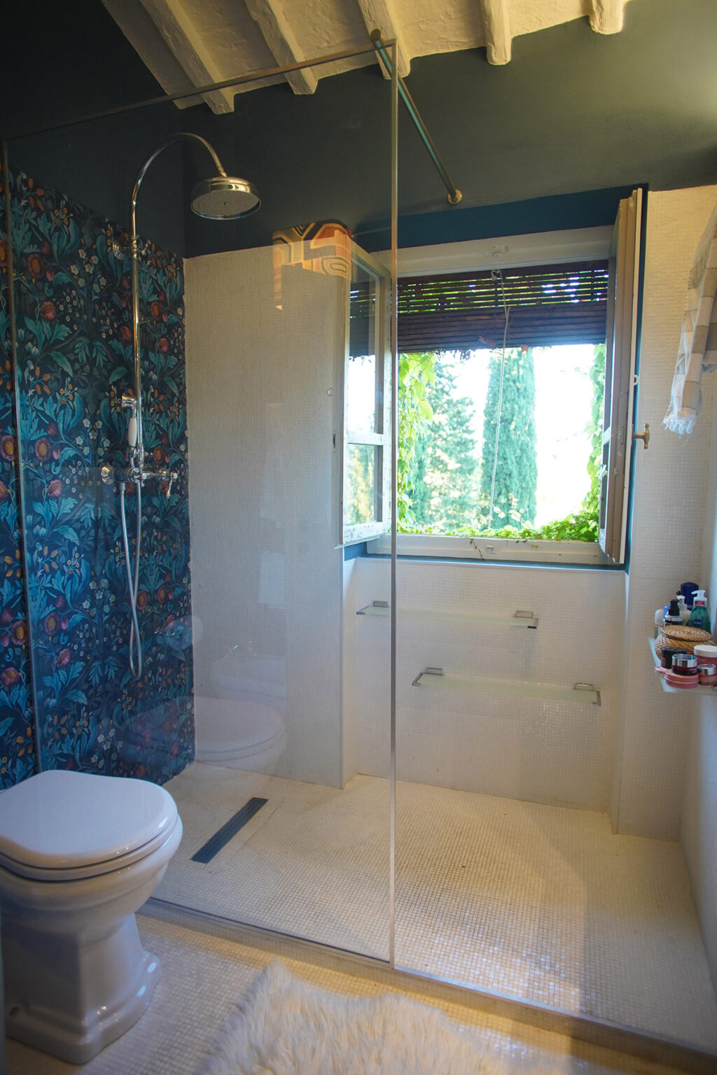 Bright and airy bathroom featuring a glass shower enclosure, a window with a scenic view of greenery, and modern fixtures. The walls are adorned with colorful tiles, enhancing the space's aesthetic appeal. | Only on SopranoVillas