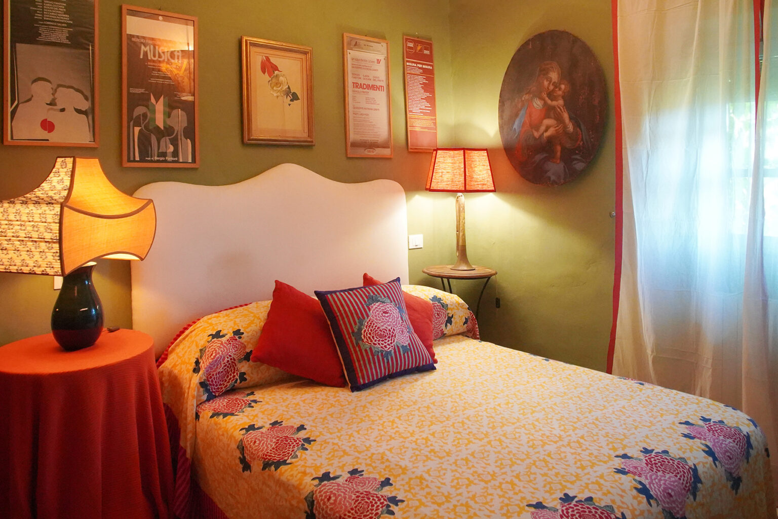 Cozy bedroom featuring a floral-patterned bedspread, decorative pillows, and vintage wall art. Soft lighting from bedside lamps enhances the inviting atmosphere, with green walls and a sheer curtain adding a touch of warmth and charm. | Only on SopranoVillas