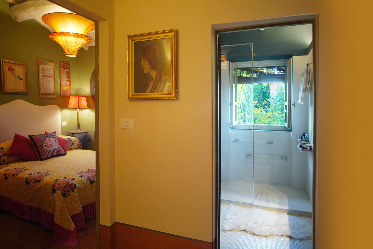 Cozy bedroom with colorful decor and a framed artwork, leading to a modern bathroom with glass shower and natural light. | Only on SopranoVillas