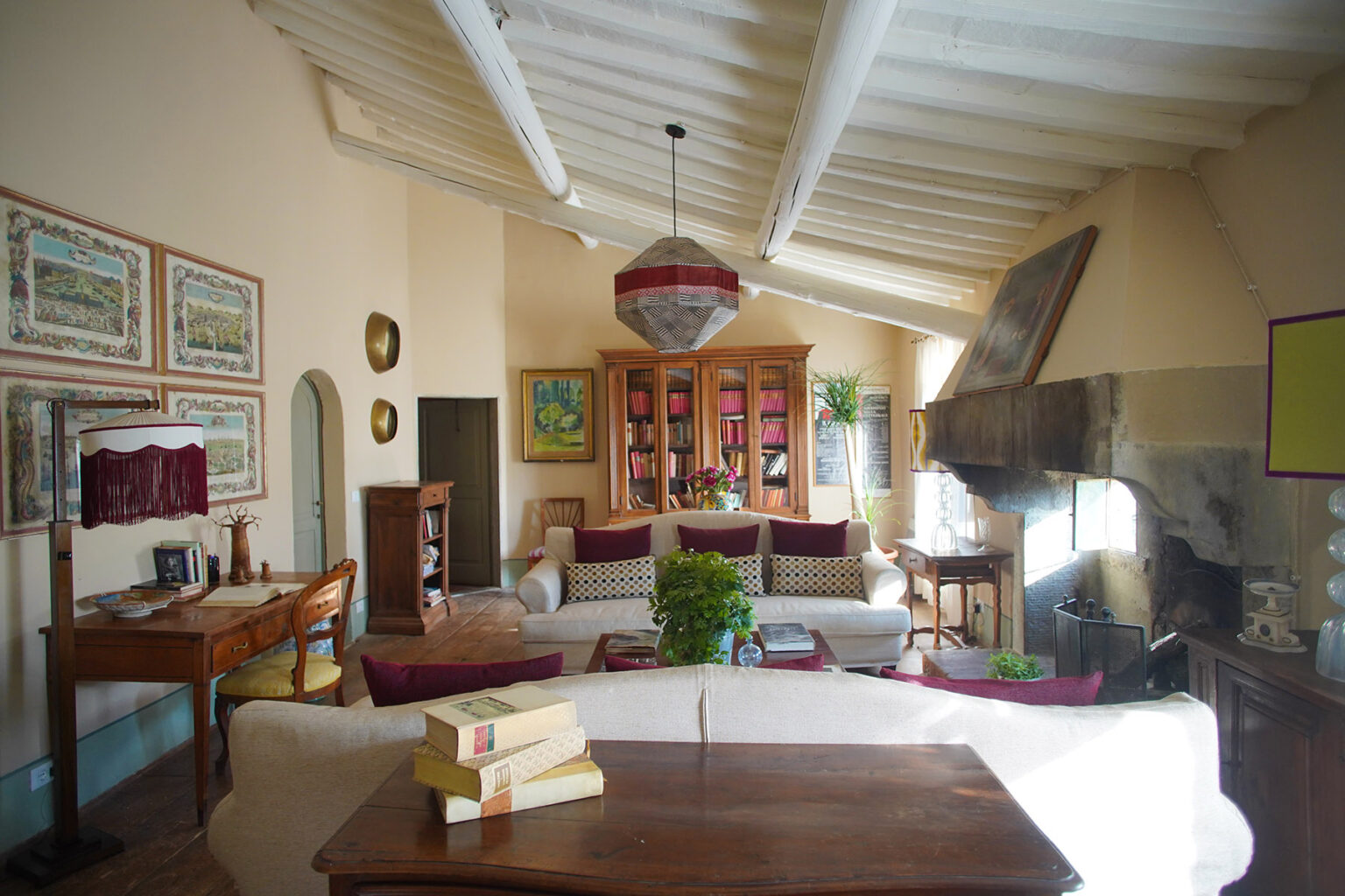 Spacious living room featuring high ceilings, a cozy seating area with plush sofas, decorative artwork on the walls, a wooden coffee table with books, and a warm ambiance created by natural light and stylish decor. | Only on SopranoVillas