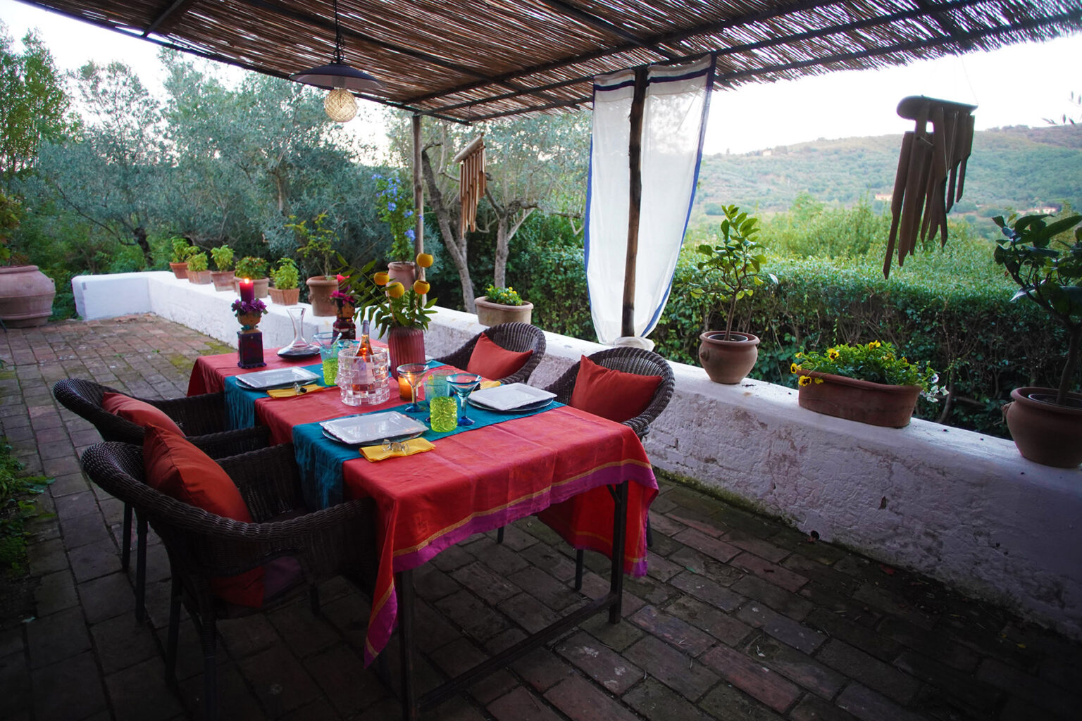 Charming outdoor dining area with a colorful table setting, surrounded by lush greenery and potted plants, ideal for al fresco meals and gatherings. | Only on SopranoVillas