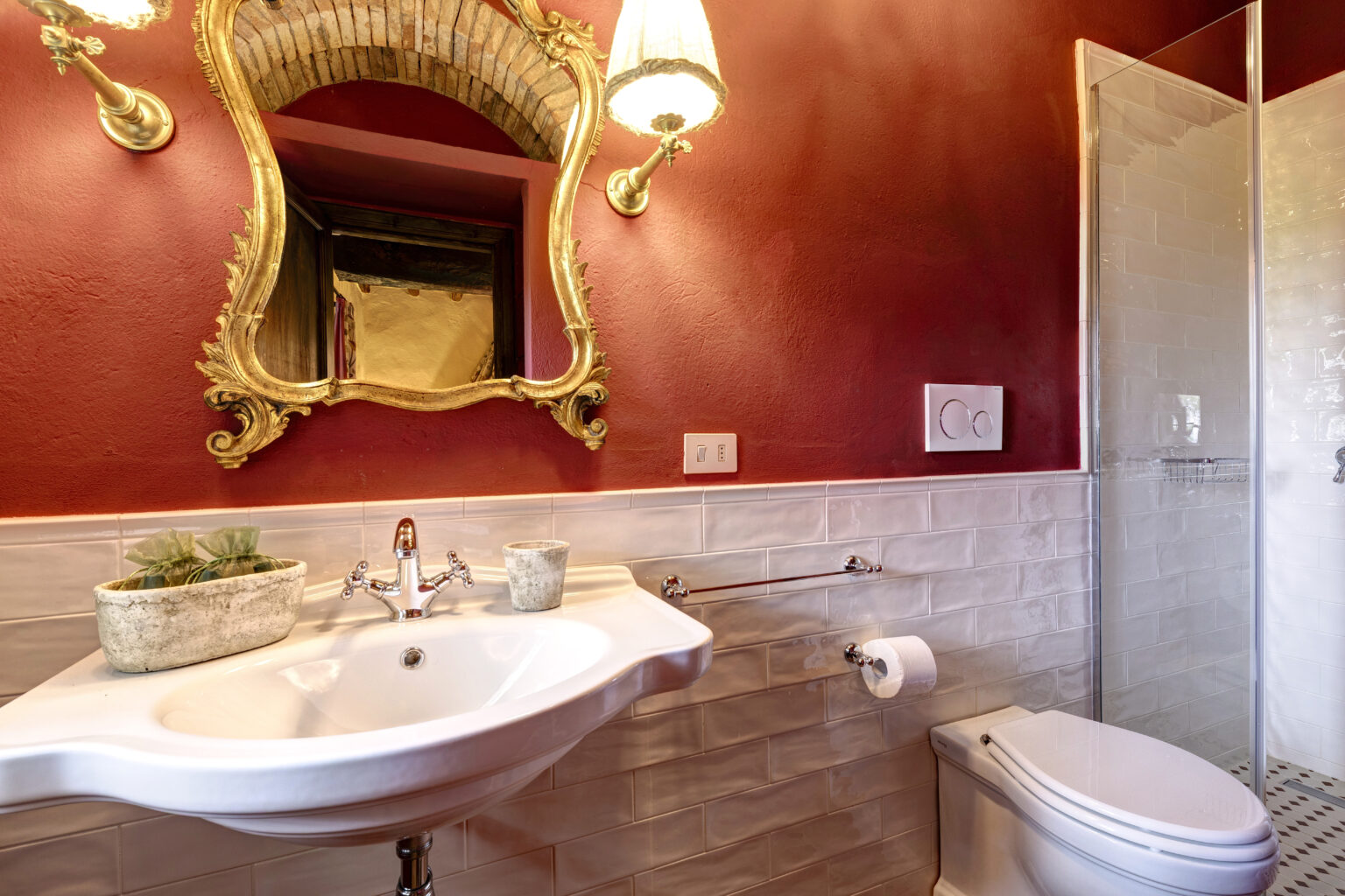Elegant bathroom interior featuring a vintage-style sink, ornate mirror, and modern shower. The walls are painted a rich red, complemented by white subway tiles and stylish fixtures, creating a sophisticated ambiance. | Only on SopranoVillas