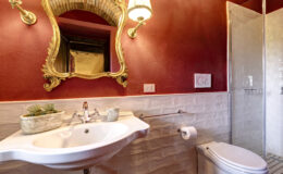 Elegant bathroom interior featuring a vintage-style sink, ornate mirror, and modern shower. The walls are painted a rich red, complemented by white subway tiles and stylish fixtures, creating a sophisticated ambiance.
