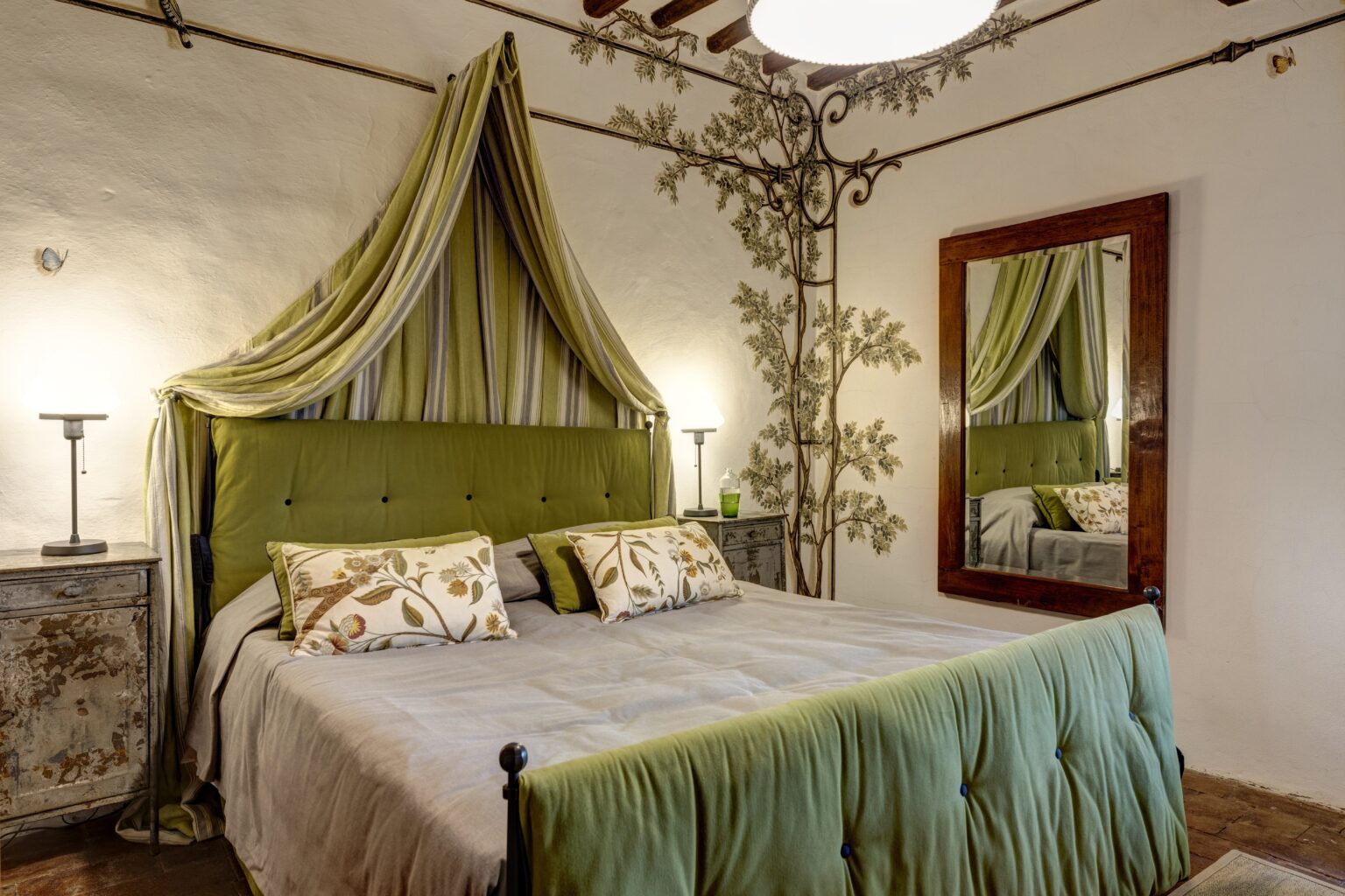 Luxurious bedroom in an Italian villa featuring elegant green decor, a plush bed with decorative pillows, stylish lighting, and a vintage mirror, ideal for a relaxing getaway. | Only on SopranoVillas