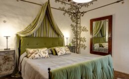 Luxurious bedroom in an Italian villa featuring elegant green decor, a plush bed with decorative pillows, stylish lighting, and a vintage mirror, ideal for a relaxing getaway.