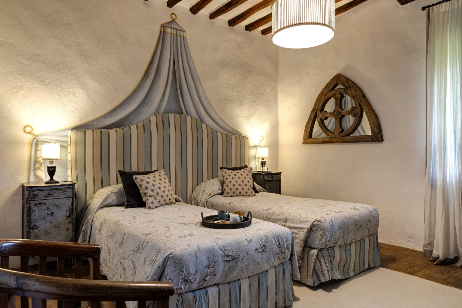 Cozy bedroom featuring two twin beds with elegant patterned bedding, a decorative headboard draped with fabric, rustic wooden accents, and soft lighting, creating a warm and inviting atmosphere. | Only on SopranoVillas