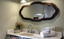 Elegant bathroom vanity featuring a vintage oval mirror, chrome faucet, and neatly rolled white towels on a marble countertop. Decorative potted plants add a touch of greenery, enhancing the serene atmosphere. Soft lighting illuminates the space, creating a cozy ambiance.