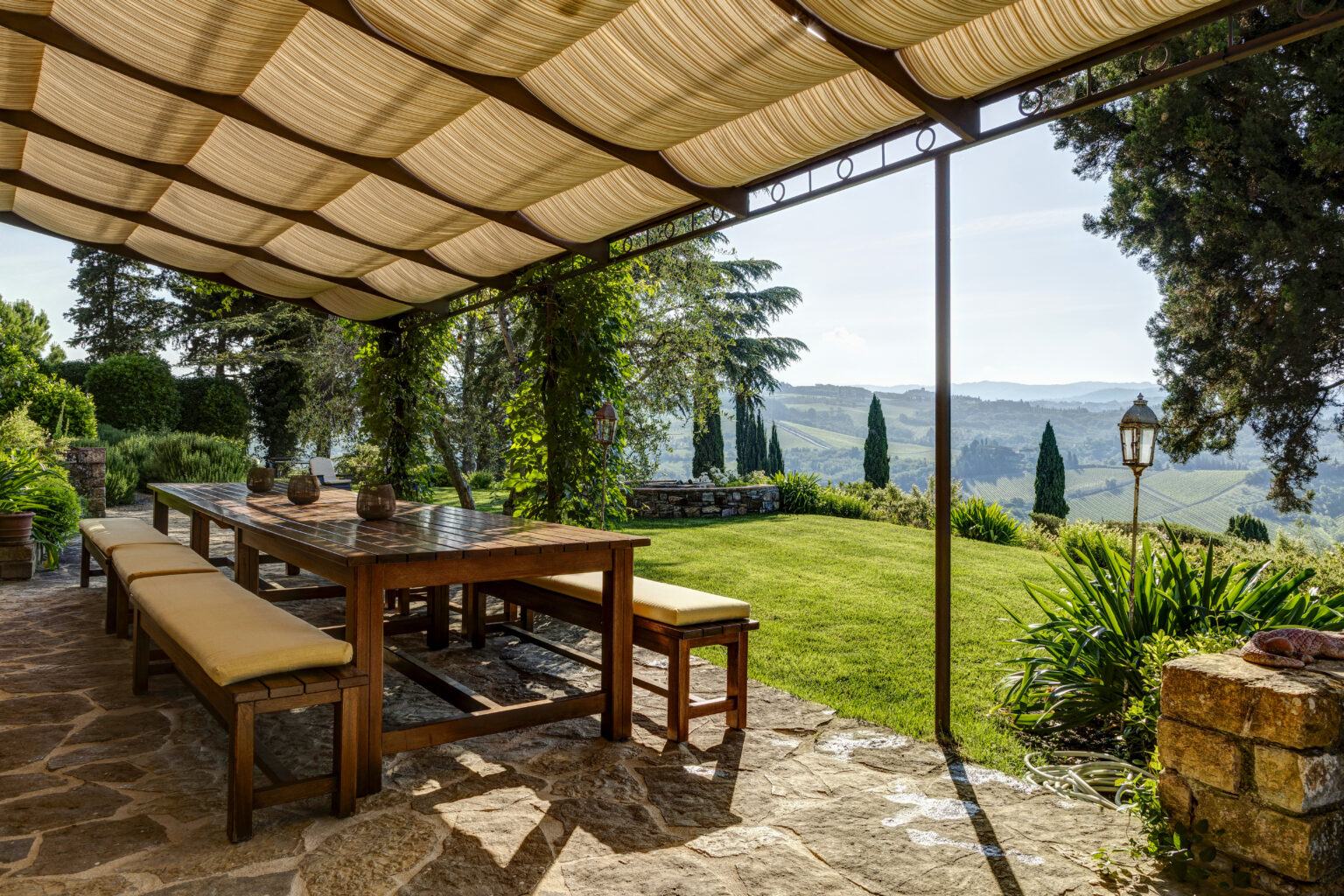 Outdoor dining area under a stylish canopy, featuring a wooden table and benches, surrounded by lush greenery and scenic views of rolling hills. Perfect for al fresco meals in a serene garden setting. | Only on SopranoVillas