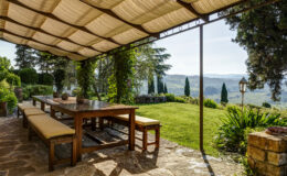 Outdoor dining area under a stylish canopy, featuring a wooden table and benches, surrounded by lush greenery and scenic views of rolling hills. Perfect for al fresco meals in a serene garden setting.