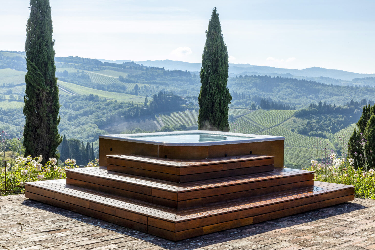 Wooden hot tub with steps overlooking lush green vineyards and rolling hills under a clear sky. Ideal for relaxation and enjoying scenic views in a tranquil outdoor setting. | Only on SopranoVillas