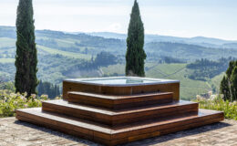 Wooden hot tub with steps overlooking lush green vineyards and rolling hills under a clear sky. Ideal for relaxation and enjoying scenic views in a tranquil outdoor setting.