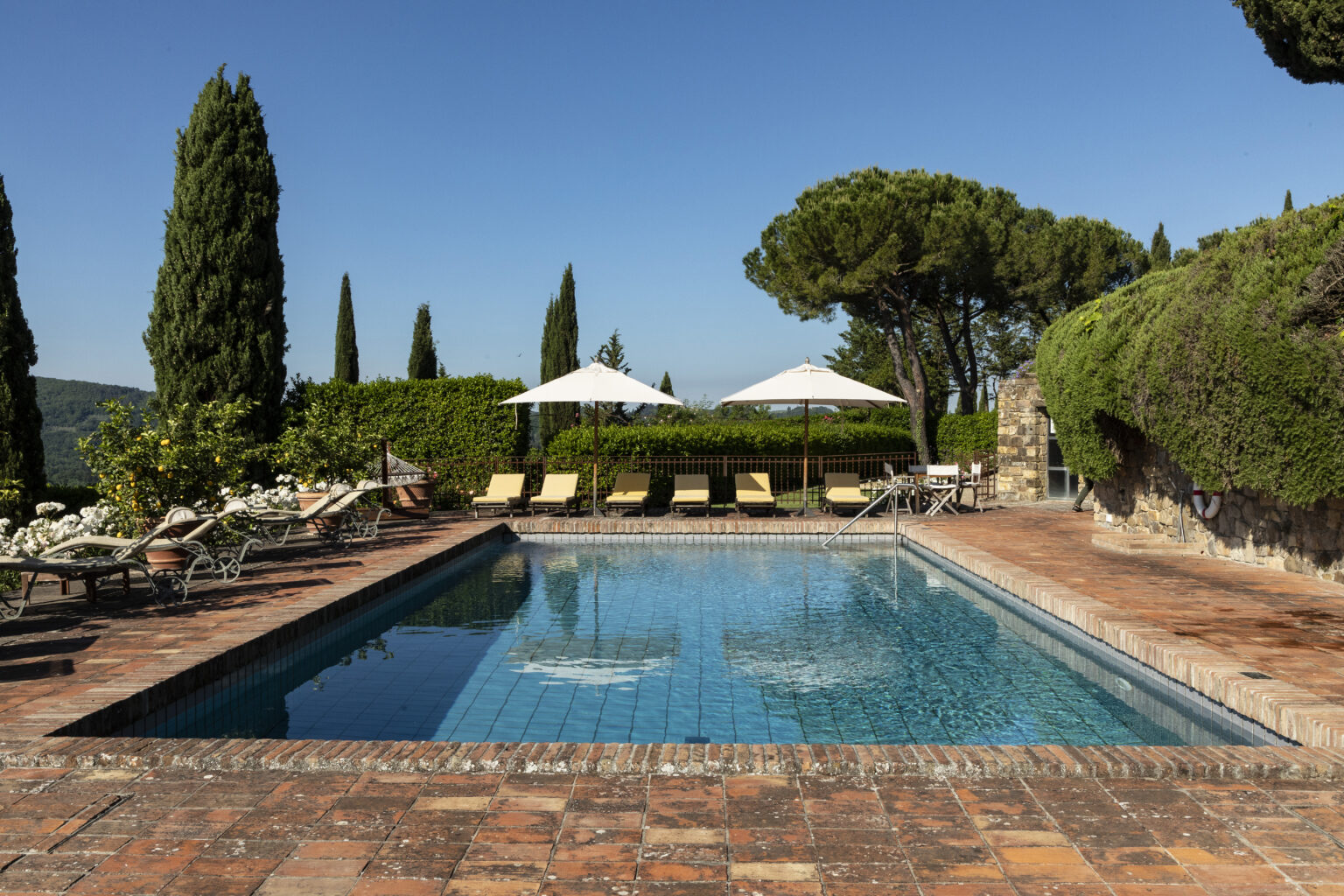 Elegant outdoor swimming pool surrounded by lush greenery and comfortable loungers, ideal for relaxation in a tranquil setting. Bright blue sky enhances the picturesque atmosphere, making it a perfect getaway destination. | Only on SopranoVillas