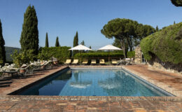 Elegant outdoor swimming pool surrounded by lush greenery and comfortable loungers, ideal for relaxation in a tranquil setting. Bright blue sky enhances the picturesque atmosphere, making it a perfect getaway destination.