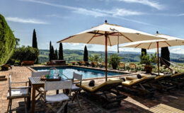 Scenic outdoor pool area with lounge chairs and umbrellas, surrounded by lush greenery and rolling hills, perfect for relaxation and leisure in a sunny setting.