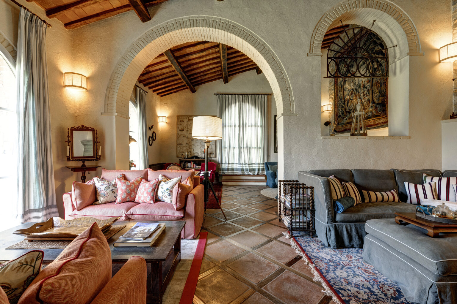Cozy living room featuring a mix of vintage and modern decor, with a coral sofa adorned with decorative pillows, a wooden coffee table, and elegant lighting. The space showcases arched doorways, textured walls, and a warm color palette, creating an inviting atmosphere. | Only on SopranoVillas