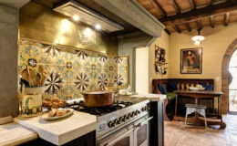 Rustic kitchen featuring a traditional gas stove, marble countertop, and colorful tiled backsplash. The space includes wooden utensils, a decorative pot, and a cozy dining area with a round wooden table and cushioned seating. Exposed wooden beams and warm lighting enhance the inviting atmosphere.