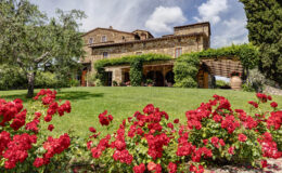 Charming stone villa surrounded by lush greenery and vibrant red roses, set against a bright blue sky with fluffy clouds, ideal for a picturesque getaway in the countryside.