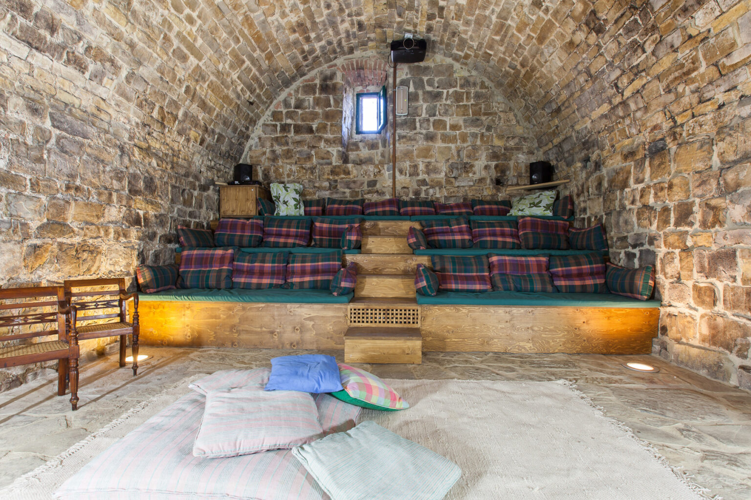 Cozy interior of a stone-walled lounge featuring tiered seating with plaid cushions, wooden accents, and soft floor pillows, creating a comfortable atmosphere for relaxation or gatherings. | Only on SopranoVillas