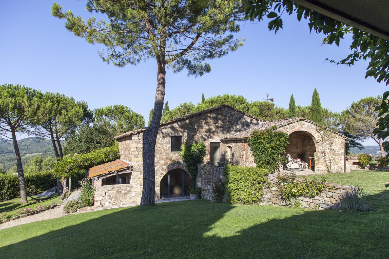 Charming stone farmhouse surrounded by lush greenery and tall pine trees in a serene landscape, ideal for vacation rentals in the countryside. | Only on SopranoVillas