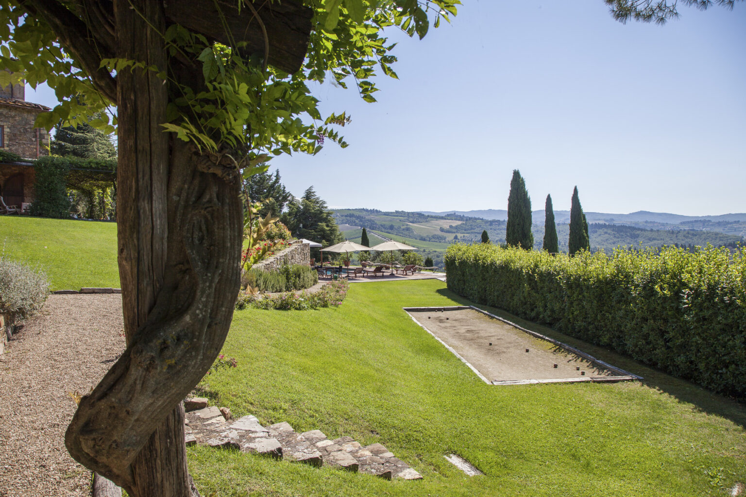 Scenic view of a well-maintained garden with lush green grass, a bocce court, and distant hills under a clear blue sky, ideal for outdoor relaxation. | Only on SopranoVillas