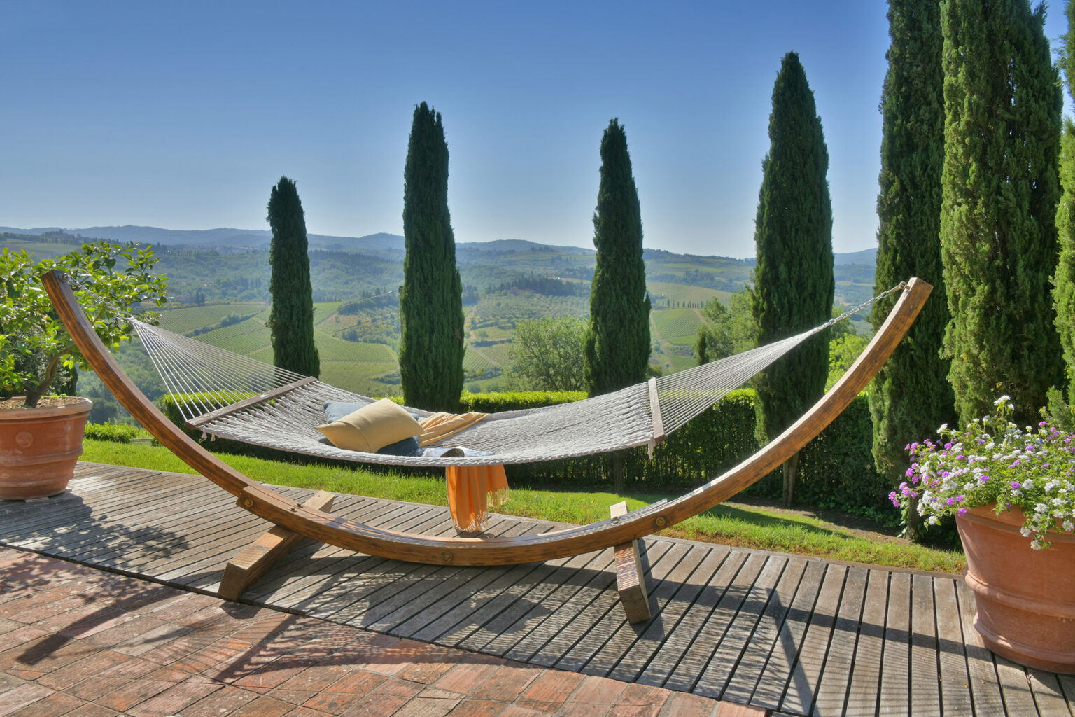 Relaxing hammock on a wooden deck overlooking rolling hills and cypress trees in a tranquil outdoor setting. Perfect for enjoying nature and unwinding in a scenic landscape. | Only on SopranoVillas