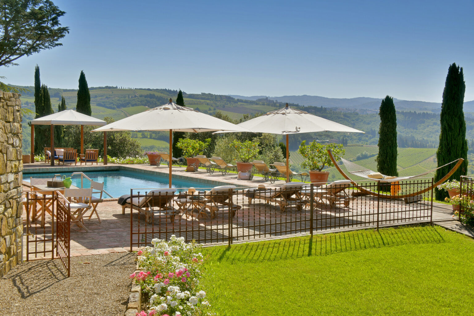Scenic outdoor pool area with lounge chairs, umbrellas, and a hammock, surrounded by lush greenery and rolling hills, ideal for relaxation and leisure in a tranquil setting. | Only on SopranoVillas