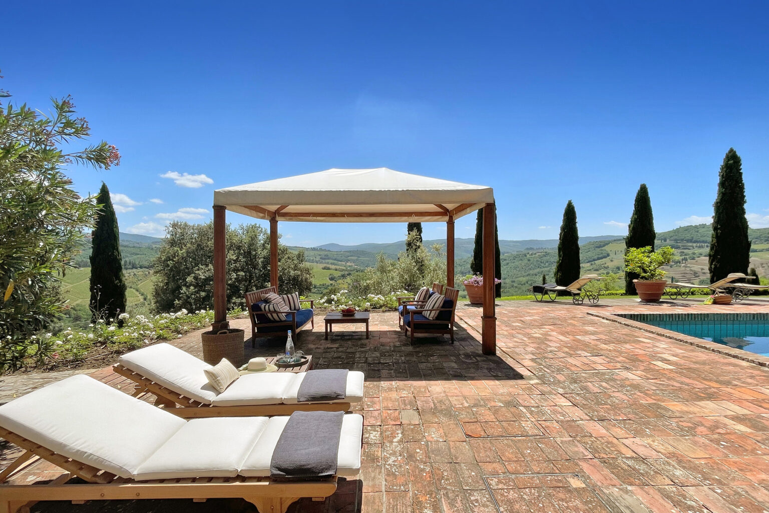 Luxurious outdoor lounge area featuring comfortable sun loungers and a shaded gazebo, surrounded by scenic hills and greenery, with a sparkling swimming pool in the background. Ideal for relaxation and enjoying nature. | Only on SopranoVillas