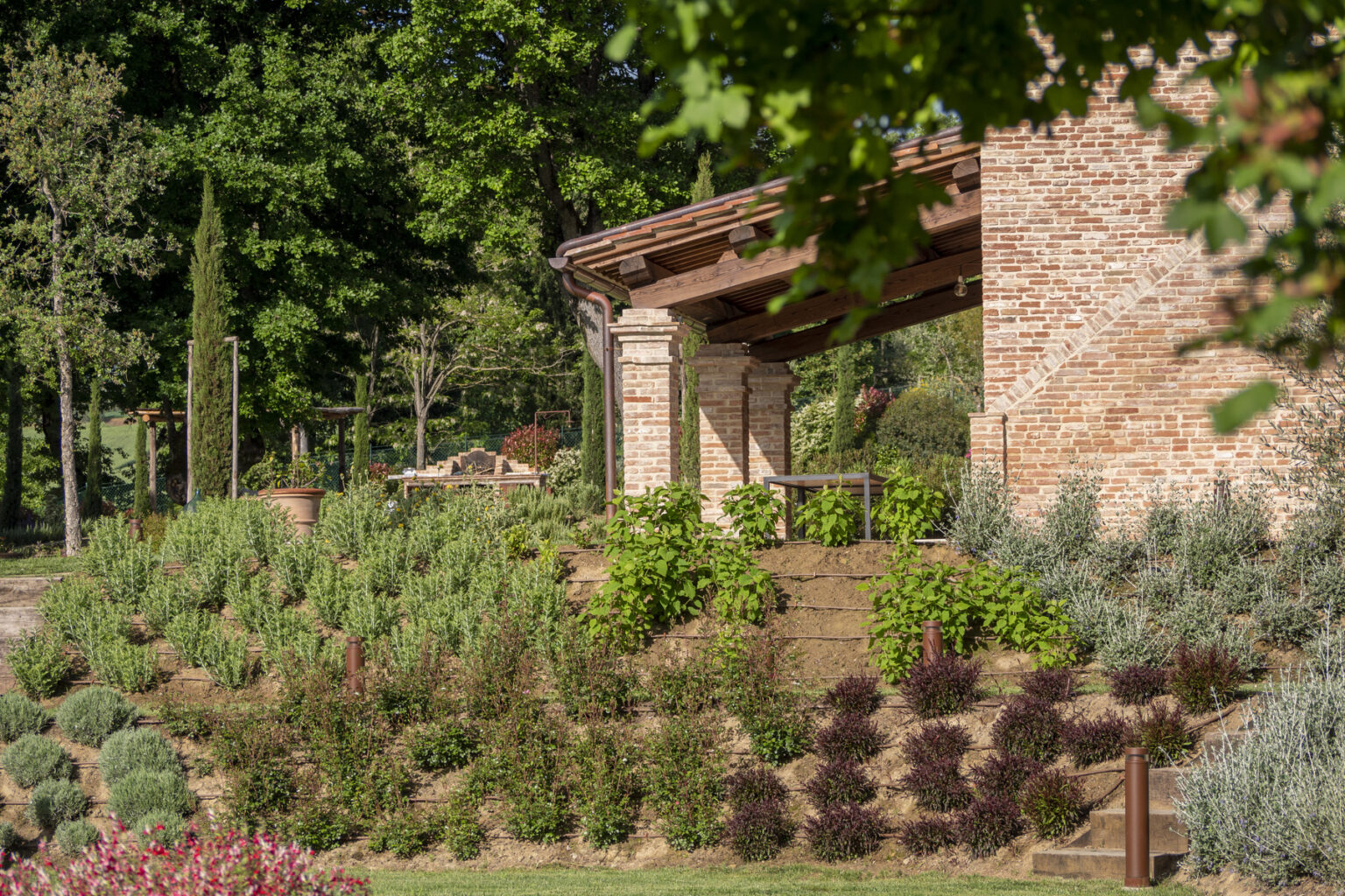 Rustic brick building surrounded by lush greenery and landscaped gardens, featuring a variety of plants, shrubs, and trees in a serene outdoor setting. | Only on SopranoVillas