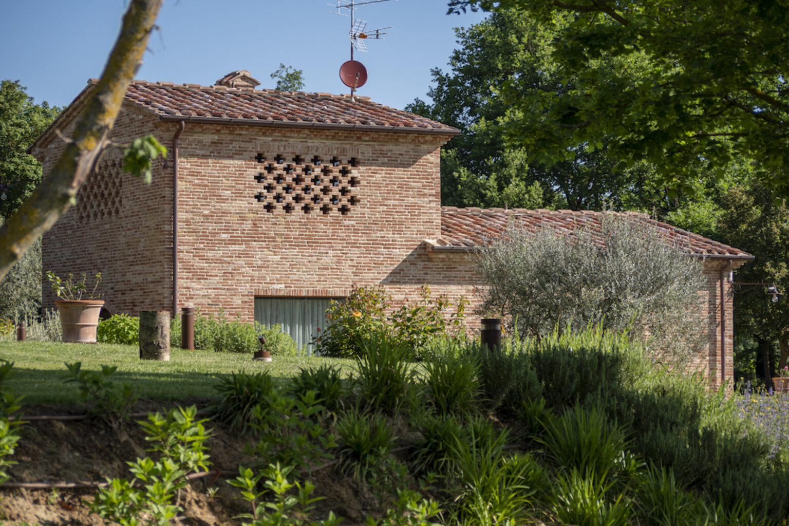 Rustic brick house surrounded by greenery, featuring a unique patterned wall, satellite dish, and well-maintained garden in a serene outdoor setting. | Only on SopranoVillas
