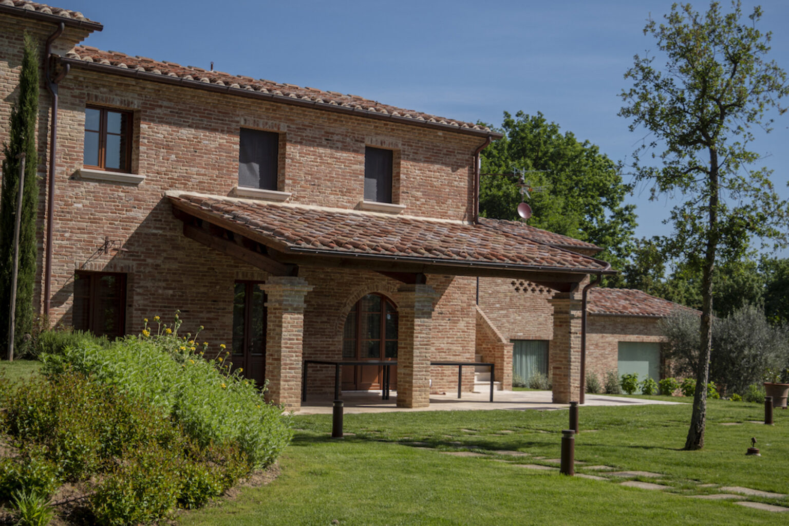 Exterior view of a rustic brick house with a tiled roof, featuring large windows and a covered porch area. Surrounded by well-maintained gardens and greenery, the property showcases a blend of traditional architecture and natural beauty. | Only on SopranoVillas