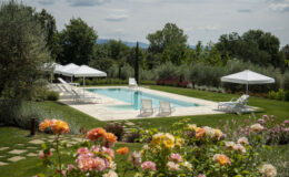 Beautiful outdoor swimming pool surrounded by lush greenery and blooming flowers, featuring white lounge chairs and umbrellas for relaxation on a sunny day. Perfect for a tranquil getaway or a luxurious retreat.