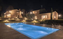 Elegant night view of a luxurious villa featuring a glowing blue swimming pool, surrounded by landscaped gardens and softly lit pathways, showcasing modern architecture and serene outdoor ambiance.